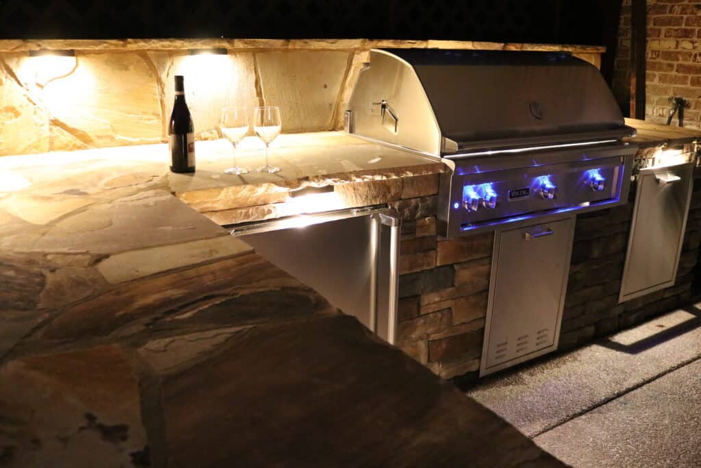 Outdoor Kitchen with stainless appliances and natural stone backsplash with lights Spring Hill