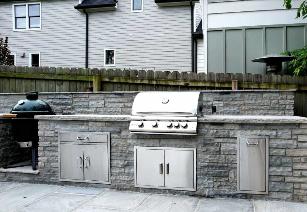 Gray natural stone outdoor kitchen with stainless appliances, green egg, and storage doors Spring Hill
